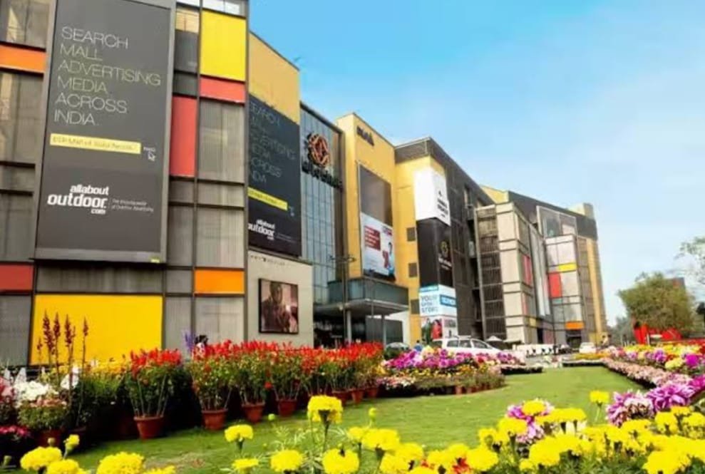 Colorful flower beds in front of a modern mall in Noida, showcasing the vibrant exterior of DLF Mall of India on a sunny day.